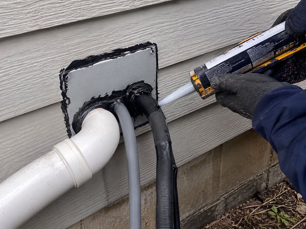 Technician sealing a utility line penetration on exterior siding with a cover plate